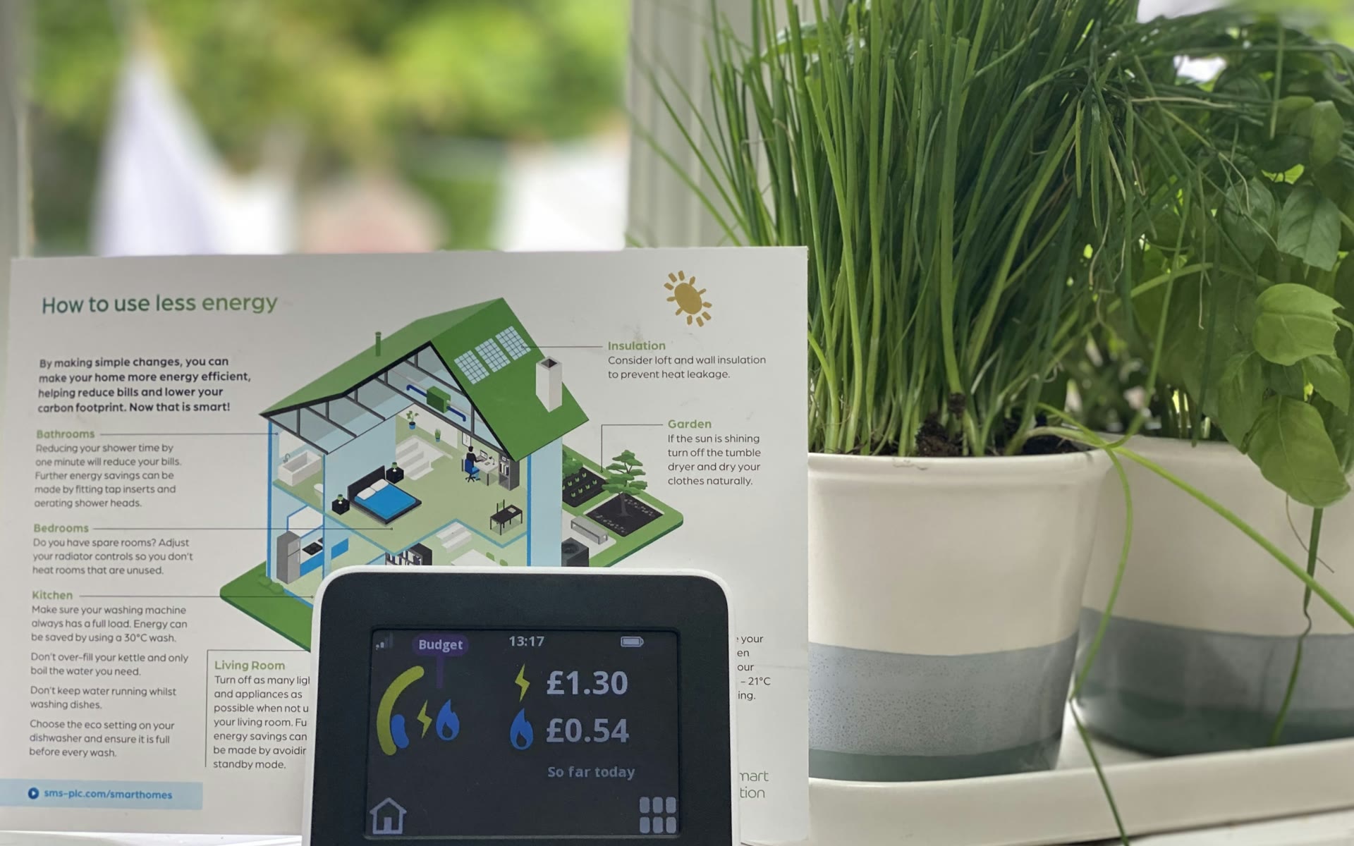 Digitales Energiemonitor-Display vor einer Informationsgrafik zum Stromverbrauch im Wohnhaus.